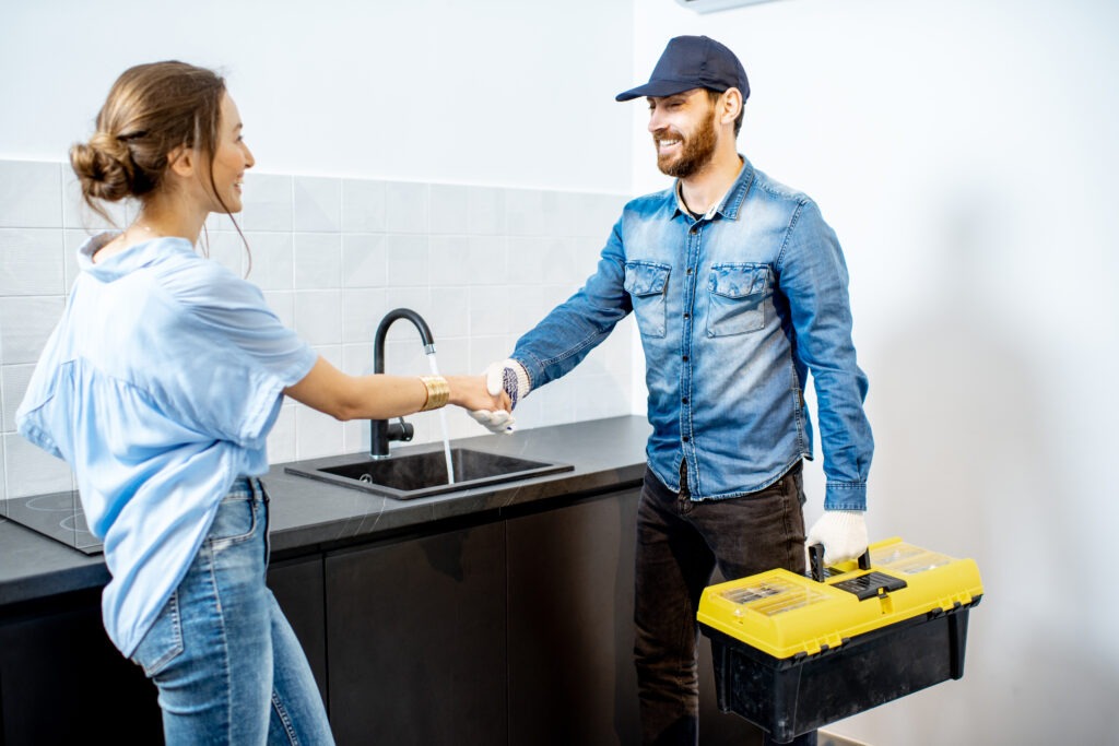 Friendly plumber in Minneapolis shaking hands with a satisfied customer in a modern kitchen. Riser Water provides expert plumbing services in Minneapolis, including emergency plumber solutions for homes and businesses.
