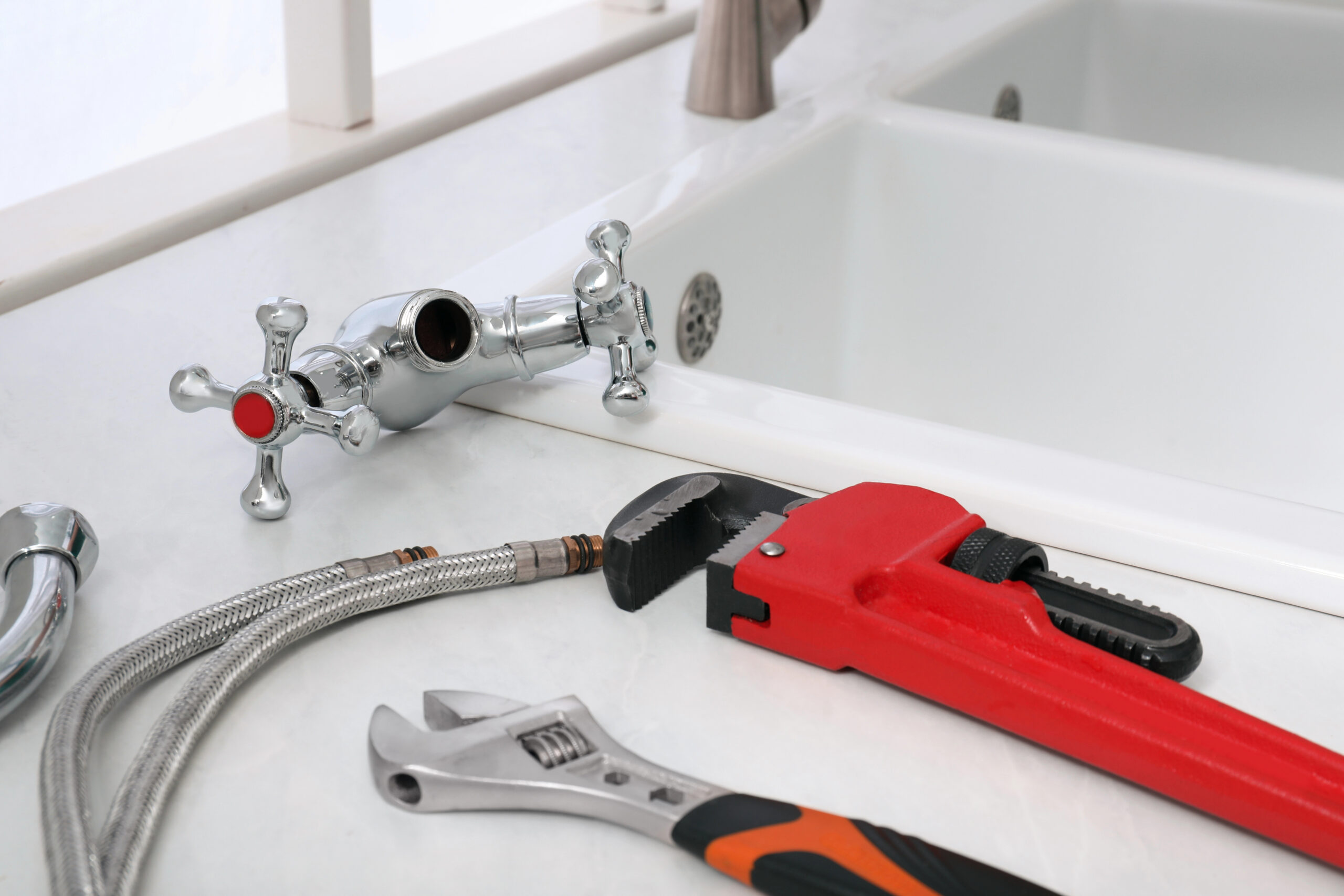 Disassembled sink faucet with plumbing tools and flexible water supply lines on a kitchen countertop, showing a repair or installation in progress.