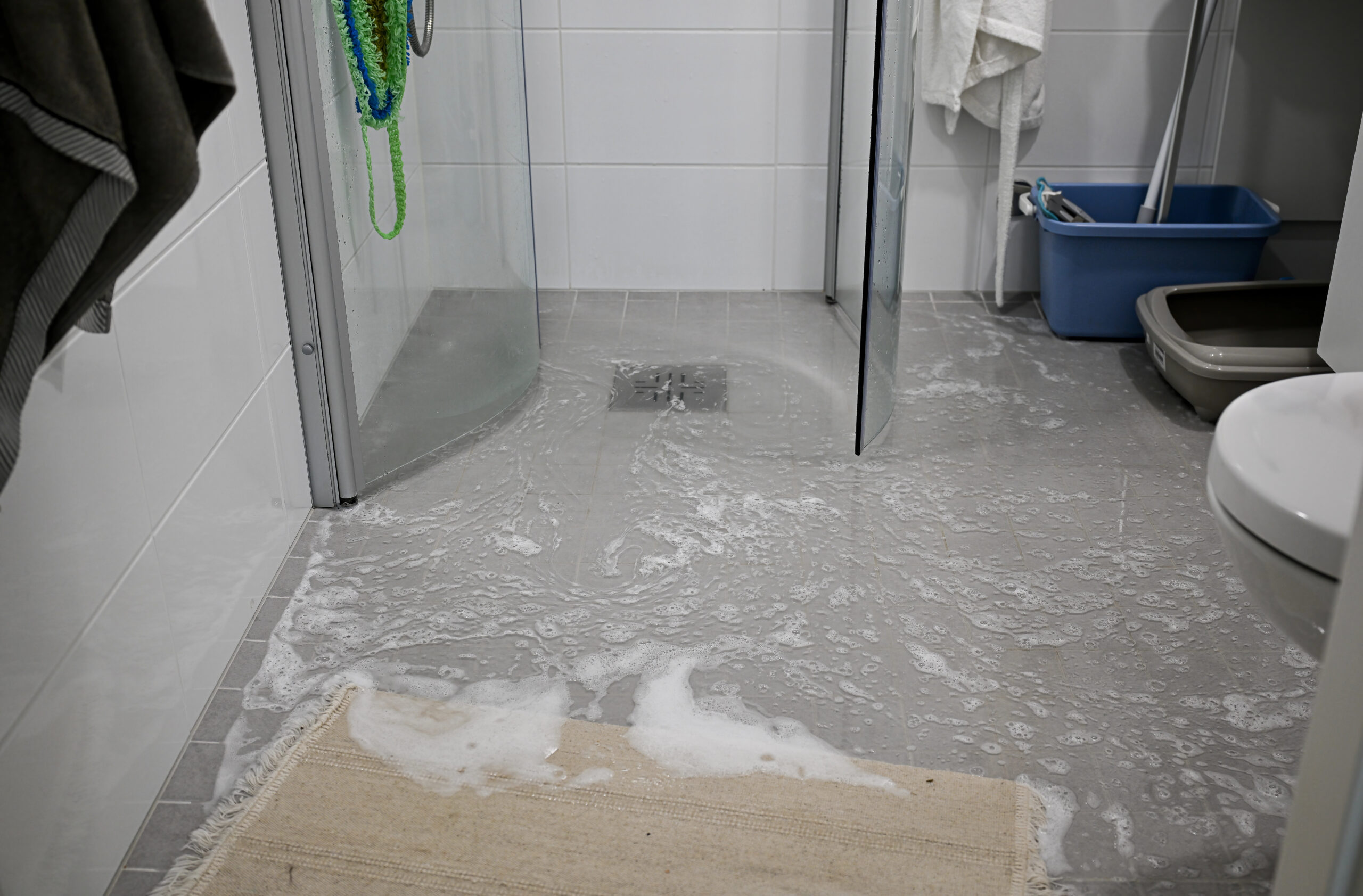Bathroom floor covered in soapy water from an overflowing shower, showing an indoor flooding and drainage issue.